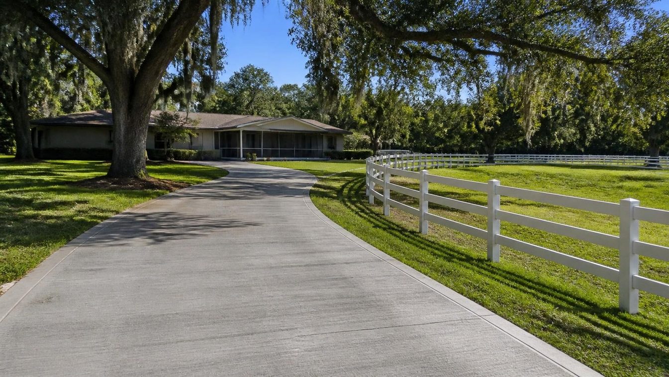 Newly poured broom-finish concrete driveway beside a Central Florida home, with a horse pasture fence beyond